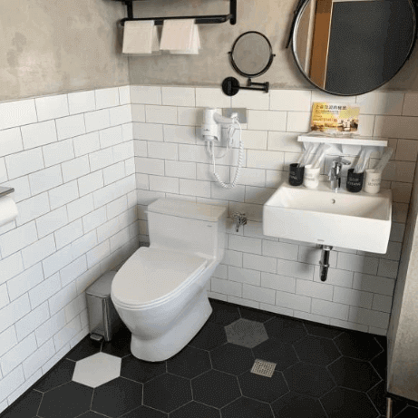 Contemporary bathroom in a hotel with white subway tiles, hexagonal black floor tiles, a wall-mounted sink, and a round mirror.