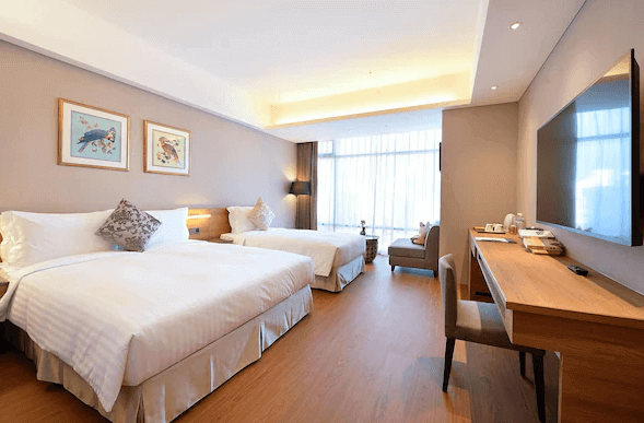 【宜蘭溫泉飯店】宜蘭悅川酒店的雙床客房，明亮的落地窗為房間帶來充足的自然光，內部設計簡潔，並且使用溫暖的木質材料。房間內擺放了一張長桌，適合商務使用或休閒閱讀，整體感覺乾淨且舒適。