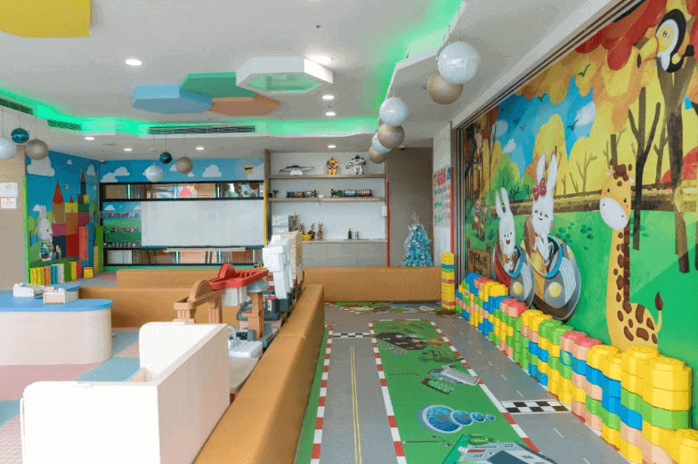 Colorful children's playroom in a hotel with vibrant wall murals of animals, interactive play areas with toys, a racetrack carpet, and a dedicated entertainment setup