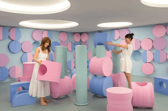 【宜蘭溫泉飯店】宜蘭館煙波大飯店一個以柔和色調為主的遊戲室，牆上和地面布滿粉藍色和粉紅色的圓形裝飾。兩位女性正用大型軟墊建構積木塔，整個空間充滿趣味和童心，適合家庭遊客和小孩玩樂。