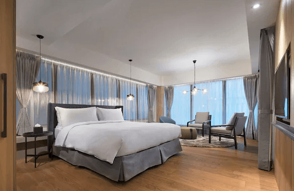 【宜蘭溫泉飯店】山形閣的現代風格客房，房內有一張大床，並搭配白色床單。房間內有多面落地窗，讓自然光充分滲入，配以簡約的家具設計如兩張舒適的椅子和小茶几，整體營造出溫馨且高雅的氛圍。