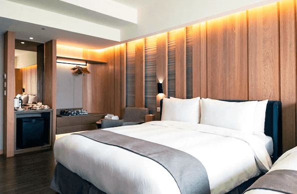 【宜蘭溫泉飯店】山形閣的客房，牆面採用暖木質裝潢設計，搭配一張舒適的大床，床頭燈光柔和。房間內的家具佈局簡約且實用，適合放鬆和休息。