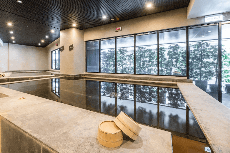 Indoor thermal spring with serene ambiance, reflecting windows showcasing greenery outside, traditional Japanese bathing buckets