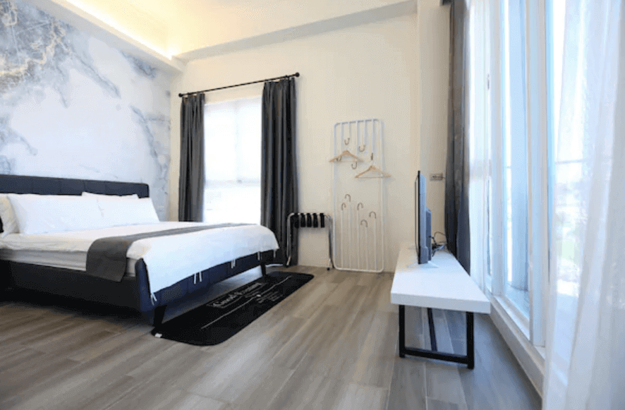 Elegant hotel room with a large comfortable bed, artistic wall mural of a world map, and ample sunlight from floor-to-ceiling windows, perfect for guests looking for a blend of comfort and style in their travel stay