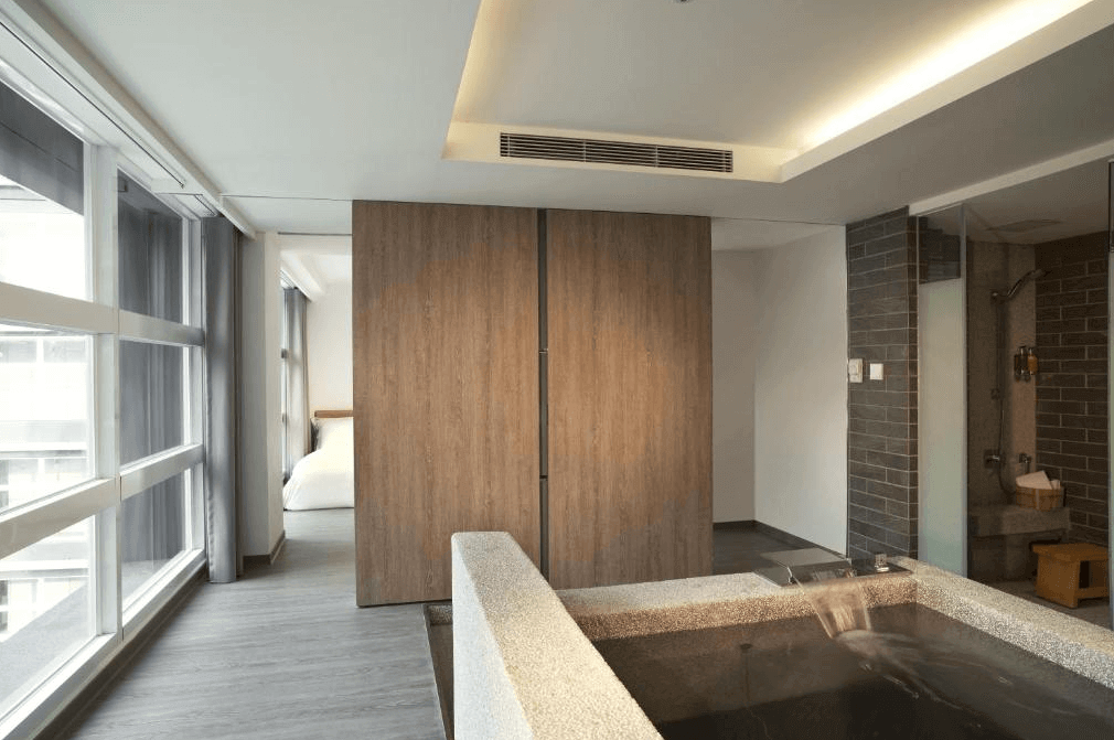 【宜蘭溫泉飯店】捷絲旅宜蘭礁溪館的一間現代化的客房，配有大窗戶和寬敞的浴缸，木質裝潢和牆壁提供了溫暖的視覺效果，浴室和睡眠區之間以簡約的木板牆隔開，增添隱私性和整體空間感。