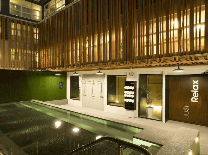 Hotel's tranquil outdoor pool area at night with mood lighting, stylish wooden deck design, and relaxing poolside shower facilities