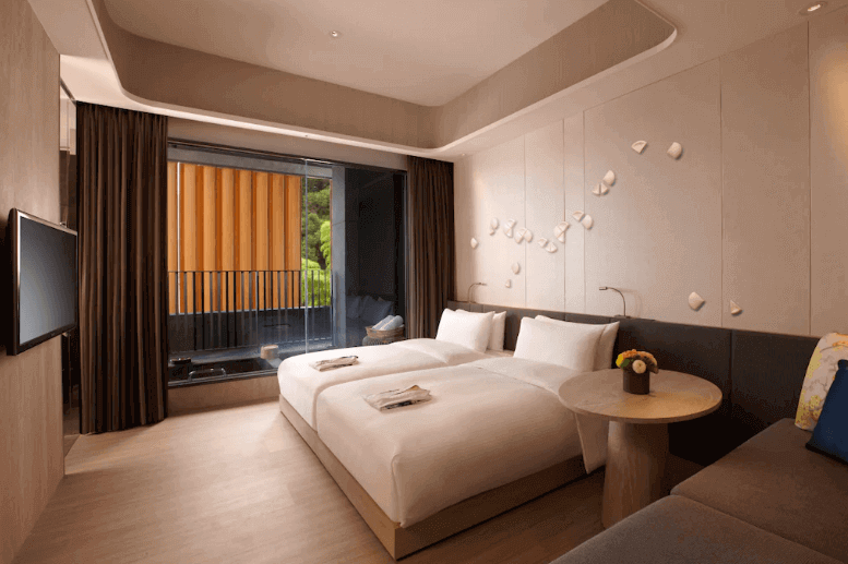 Modern hotel room with a king-sized bed, clean linen, contemporary decor with wall art, flat-screen TV, and large window overlooking the balcony with lush greenery