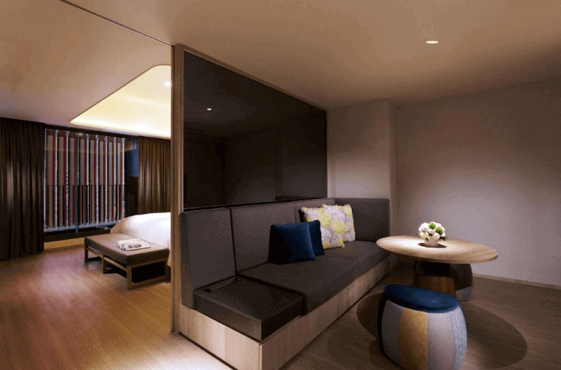 Stylish hotel suite featuring a cozy sitting area with plush sofas, chic throw pillows, a wooden coffee table, and minimalistic interior design with warm lighting