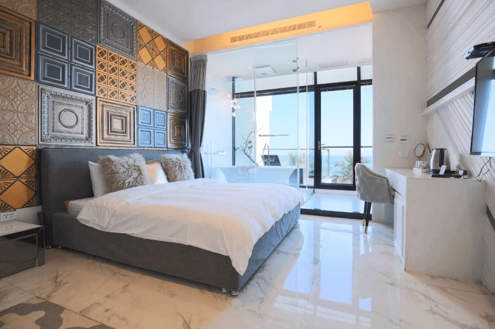 【花蓮市海景住宿】漫漫日出的客房擺放了一張雙人床，牆面使用復古金屬格紋裝飾，呈現出獨特的質感。房內有通向陽台的玻璃門，讓自然光充滿整個房間，並可享受室外海景。房內還設有辦公桌和茶具，適合休閒和放鬆。