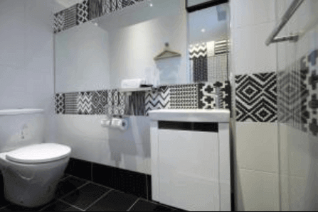 漫漫日出的浴室採用黑白幾何花紋的磁磚裝飾牆面，增添了視覺層次感。浴室內部設有馬桶和洗手台，搭配大面積鏡子，整體風格簡潔而現代，營造出時尚的氣氛。