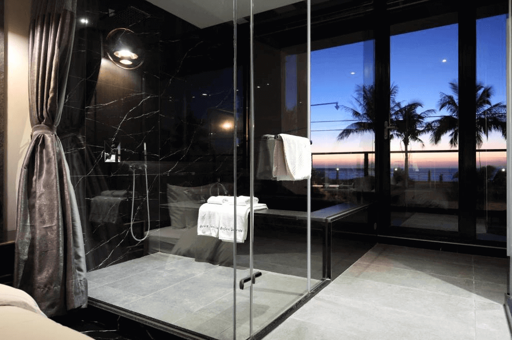 【花蓮市海景住宿】漫漫日出的浴室以深色大理石牆面為設計主題，搭配玻璃淋浴間，營造出豪華的氛圍。透過窗戶可以欣賞到美麗的海邊夜景，是放鬆身心的理想空間。
