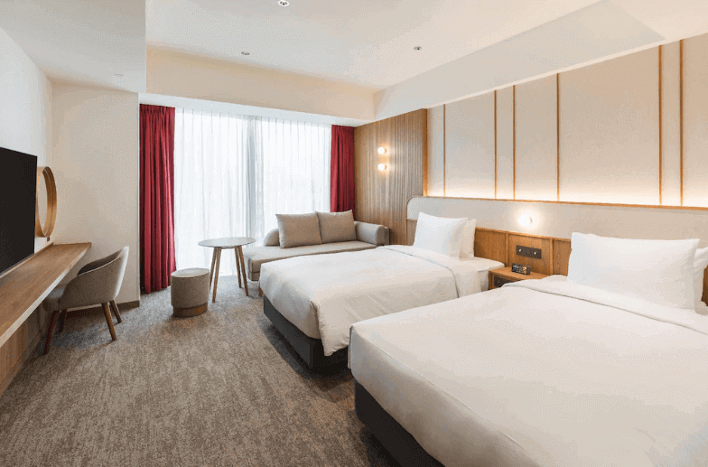 【台北親子飯店】相鐵飯店台北西門的雙床房，房內配有兩張單人床、沙發座椅和落地窗，設計簡約且明亮，適合商務或休閒旅行者入住。