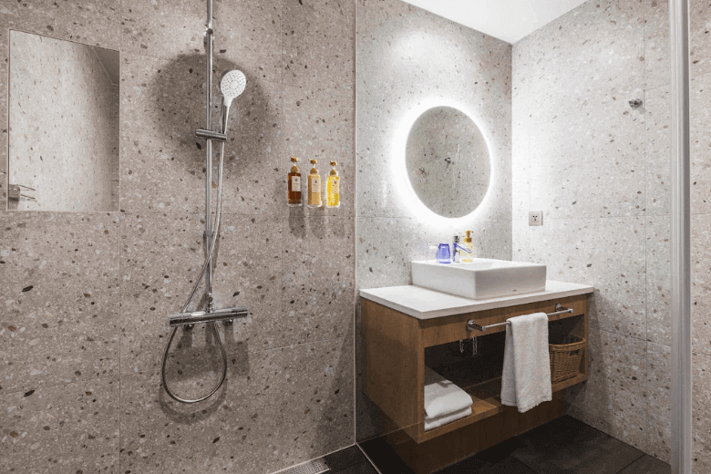 【台北親子飯店】相鐵飯店台北西門的衛浴空間，牆面採用大理石風格設計，配備圓形LED化妝鏡、獨立淋浴設備，以及精緻的洗手檯面，提供舒適的使用體驗。