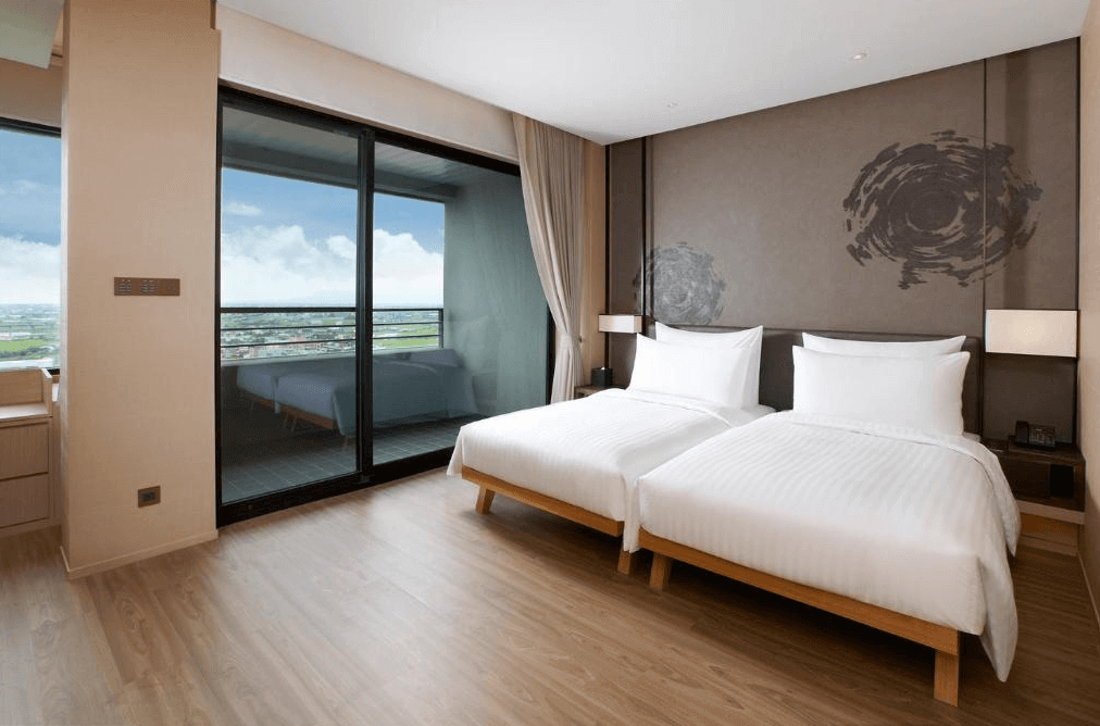 【宜蘭溫泉飯店】礁溪寒沐酒店的現代簡約風格的雙床房，房間內設有兩張白色床單的雙人床，牆面上有抽象的藝術圖案裝飾。房間連接一個陽台，落地窗外可以看到晴朗的天空和遠方的景色，營造出開闊的感覺。