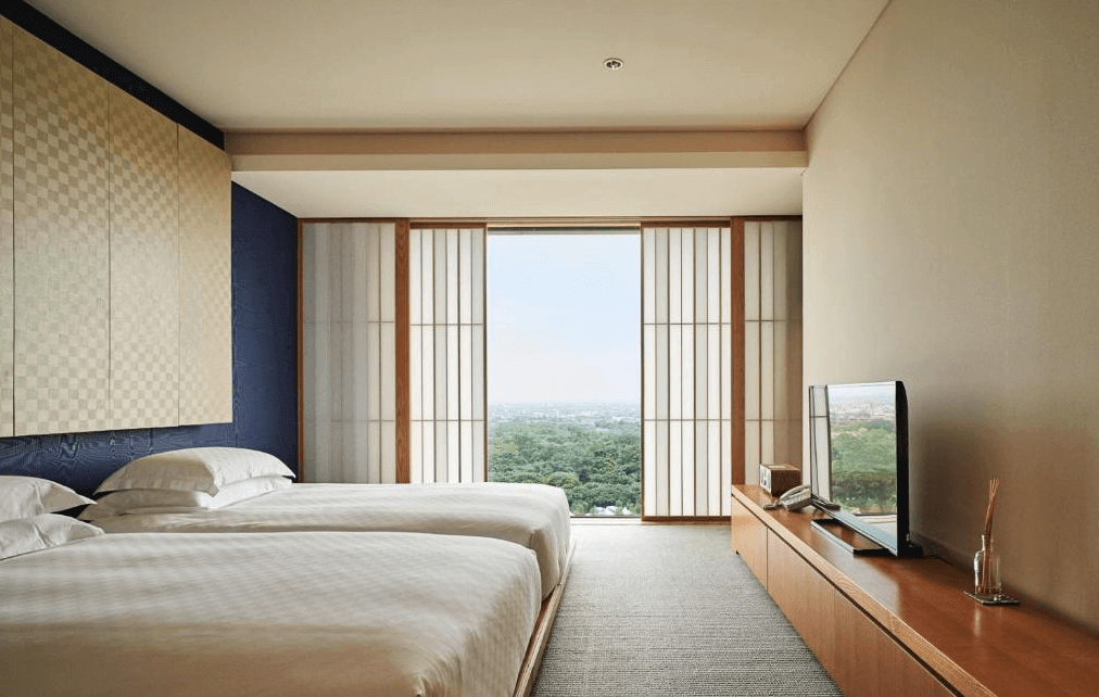 【宜蘭溫泉飯店】礁溪老爺酒店的日式風格的客房，房間內設有兩張簡約的雙人床，靠牆擺放，牆上有細緻的木質裝飾。房間的窗戶可俯瞰戶外的自然景觀，整體設計以簡潔、自然為主，配合淡雅的木色和大窗戶，讓人感覺平靜放鬆。