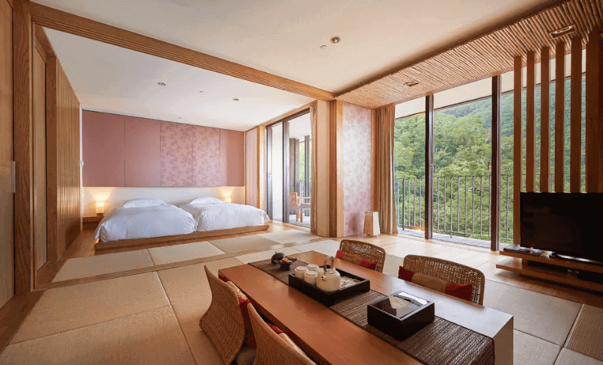 Traditional Japanese ryokan room with futon bedding and low table, offering a serene mountain view through large window