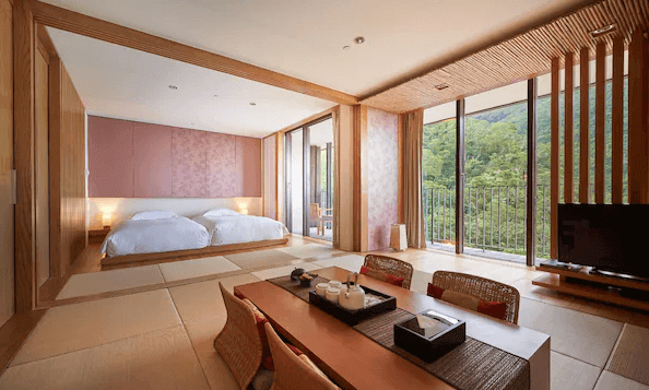 【宜蘭溫泉飯店】礁溪老爺酒店的傳統日式風格的客房，內部鋪設榻榻米，房間中央擺放著一張矮桌，桌上放有茶具，營造出和式的茶道氛圍。床區設有兩張床，後方是落地窗，窗外可以看到青山綠景，充滿自然氣息。