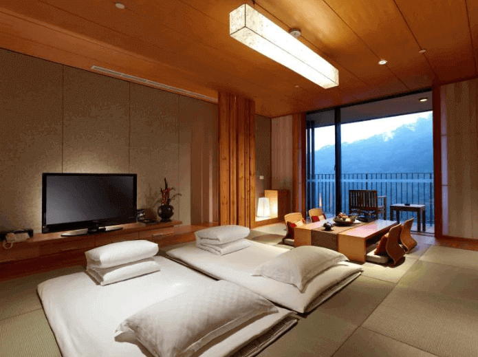 Spacious Japanese-style hotel room with tatami floors and sliding doors opening to a balcony with mountain views