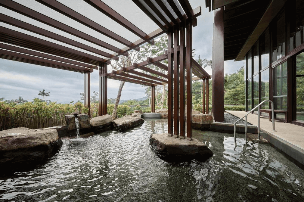 【宜蘭溫泉飯店】礁溪老爺酒店的戶外溫泉池區，溫泉池由自然石塊圍繞，並設有流水和樹木景觀。池邊的木質架構設計別緻，與周圍的自然環境相融合，讓住客享受舒適的戶外溫泉體驗。