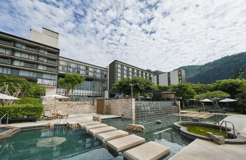 Outdoor hot spring pools at a luxury hotel, with natural stone features and lush greenery, set against a mountain backdrop
