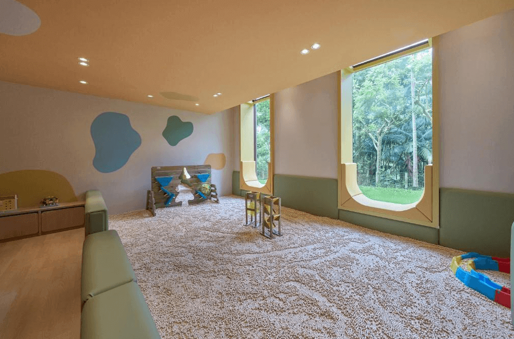【宜蘭溫泉飯店】礁溪老爺酒店的一個適合兒童的室內遊戲區，地面覆蓋著一層小顆粒的軟墊，提供安全的玩耍環境。遊戲區內有一些攀爬和玩具設施，大窗戶讓自然光充滿整個空間，並可以看到戶外的綠意景觀，整體氛圍明亮且充滿趣味。