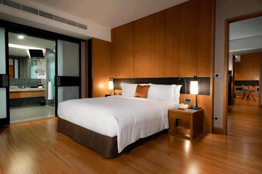 【宜蘭溫泉飯店】蘭城晶英酒店的一間現代化且溫馨的客房，房間內的主色調為木質暖色，配備舒適的大床，旁邊有兩個床頭燈和簡約的床頭櫃。床後方是木質牆板，增添了房間的溫暖感。客房的浴室通過滑動門與睡眠區隔開，浴室內設有寬敞的盥洗區。
