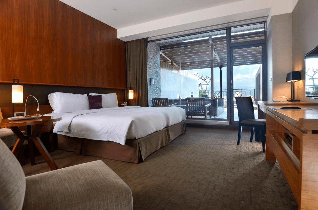 【宜蘭溫泉飯店】蘭城晶英酒店的另一間高級客房，設計現代且舒適。床旁是大型落地窗，連接室外陽台，陽台配有露天座椅。房間內有一張大床和一張書桌，整體空間寬敞且帶有自然光。