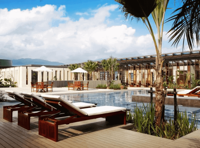 Rooftop swimming pool at a high-end hotel with lounging area, palm trees, and panoramic mountain views