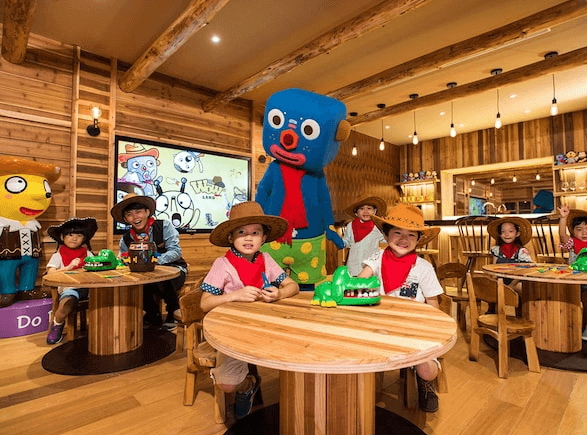 【宜蘭溫泉飯店】蘭城晶英酒店的兒童遊樂區，室內木質裝潢風格，桌椅以圓形木製為主，空間內充滿卡通裝飾，並有可愛的卡通人物模型供小孩互動。多名孩子正圍坐在桌旁，參加各式遊戲和活動，環境充滿歡樂氛圍。