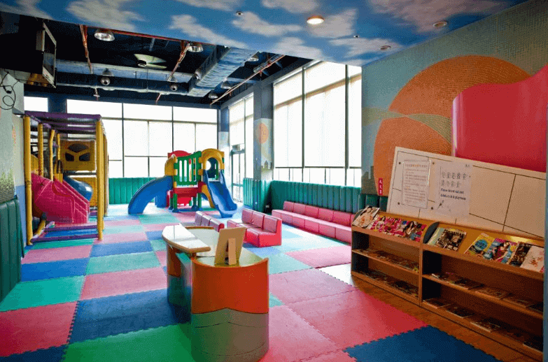 "台北親子飯店"【陽明山親子住宿】陽明山天籟渡假酒店的室內兒童遊樂區，地面鋪設柔軟的拼接墊，設有溜滑梯、攀爬架、書架以及座位區。牆上裝飾著活潑的壁畫，天花板為藍天白雲設計，營造出適合孩子們玩耍的安全且歡樂的環境。