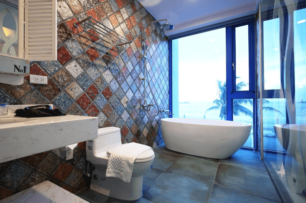 【花蓮市海景住宿】具有獨特拼貼設計的浴室，配有現代化的設施和落地窗，可以欣賞到海景。白色的浴缸和洗手台與色彩斑斕的牆面形成鮮明對比，增添了視覺上的趣味性