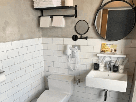 【花蓮市海景住宿】七星潭泥作輕旅民宿的浴室設計簡約，牆面使用工業風水泥搭配白色磚牆，提供明亮清新的感覺，設備齊全且布置實用，包括圓形鏡子與整潔的洗手台，細節處體現貼心設計。