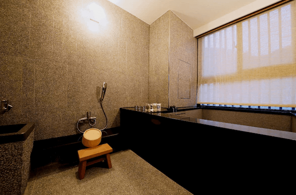 北投亞太飯店私人浴室：一間設有現代設計風格的私人浴室，內有黑色石製浴缸和淋浴區。浴室牆壁為灰色石材，提供木質椅子和浴室用品，光線柔和，設計簡約