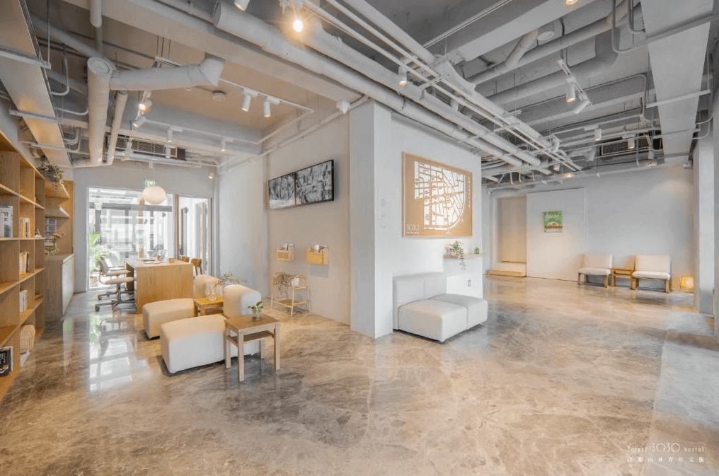 【玉里住宿】山鄰山林青年文旅的公共區域，配有舒適的白色沙發和木質書架，牆上掛有藝術裝飾，天花板裸露的管道設計，營造出開放而舒適的社交空間。