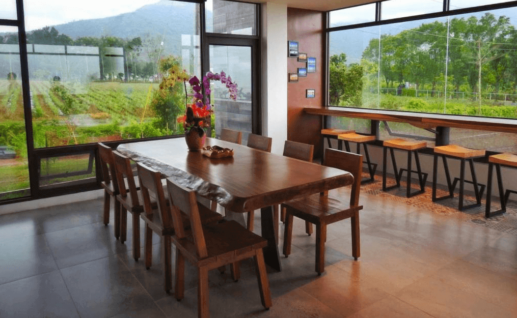 【鹿野住宿】御來光民宿的用餐區配有長木桌和多個座椅，設有大片窗戶面向戶外的田野，提供明亮的自然光線和舒適的用餐環境。