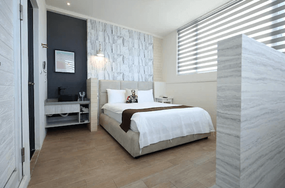 【花蓮市海景住宿】微藍海岸海景夜市電梯民宿的臥室，設有一張舒適的雙人床，床頭背景牆採用淺灰色和白色的條紋設計。房間內有大型窗戶提供充足的自然光，整體氛圍明亮且溫馨