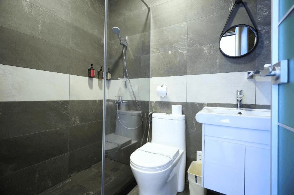 【花蓮市海景住宿】微藍海岸海景夜市電梯民宿的浴室，配有玻璃淋浴間和簡約的白色洗手台。牆面採用灰白色調的瓷磚設計，整體風格時尚且乾淨