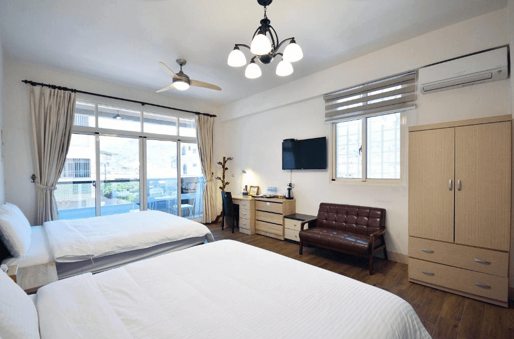 【美濃住宿】望峰息心民宿的民宿房間，房內配有兩張雙人床，牆上安裝了空調和電視。房間內還設有衣櫃和小沙發，窗外可看到陽台的景色，整體佈置簡約而舒適。