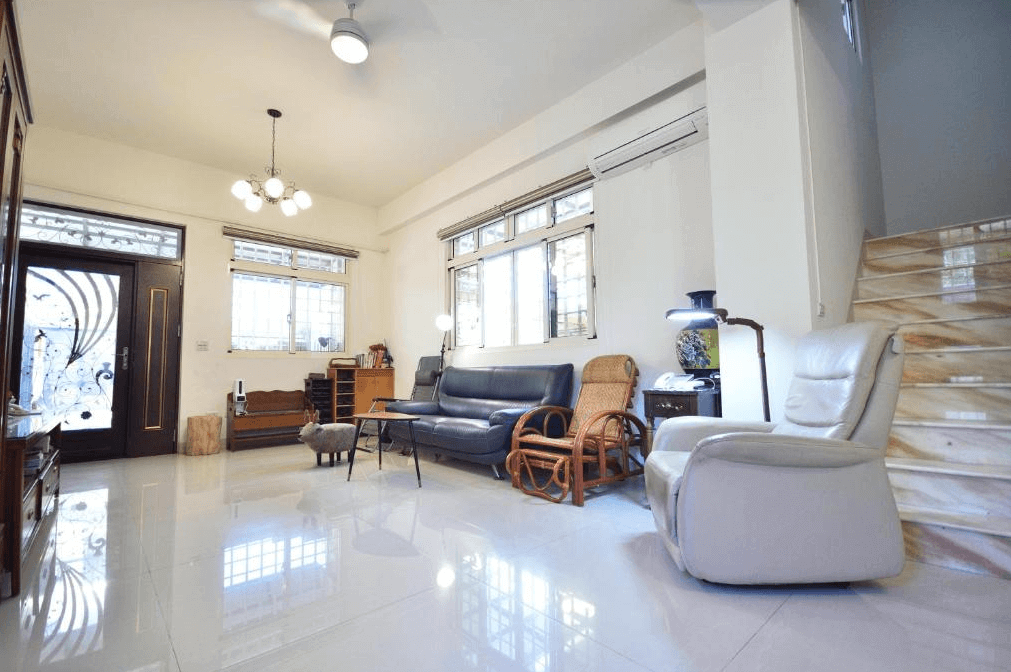 【美濃住宿】望峰息心民宿的客廳區域，配有黑色皮沙發、藤製椅子和白色皮椅。房間內裝飾簡潔明亮，樓梯通往上層，並設有大型窗戶和充足的自然光。