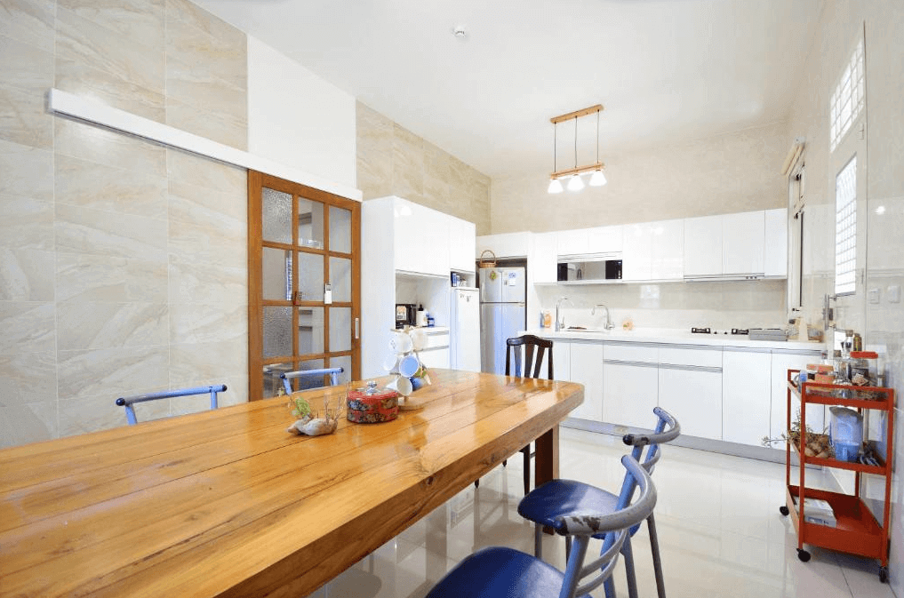 【美濃住宿】望峰息心民宿的廚房和餐廳區域，配有大木餐桌和多張椅子。廚房設備齊全，白色的櫥櫃和牆磚使整個空間顯得乾淨整潔，適合家庭用餐和烹飪。