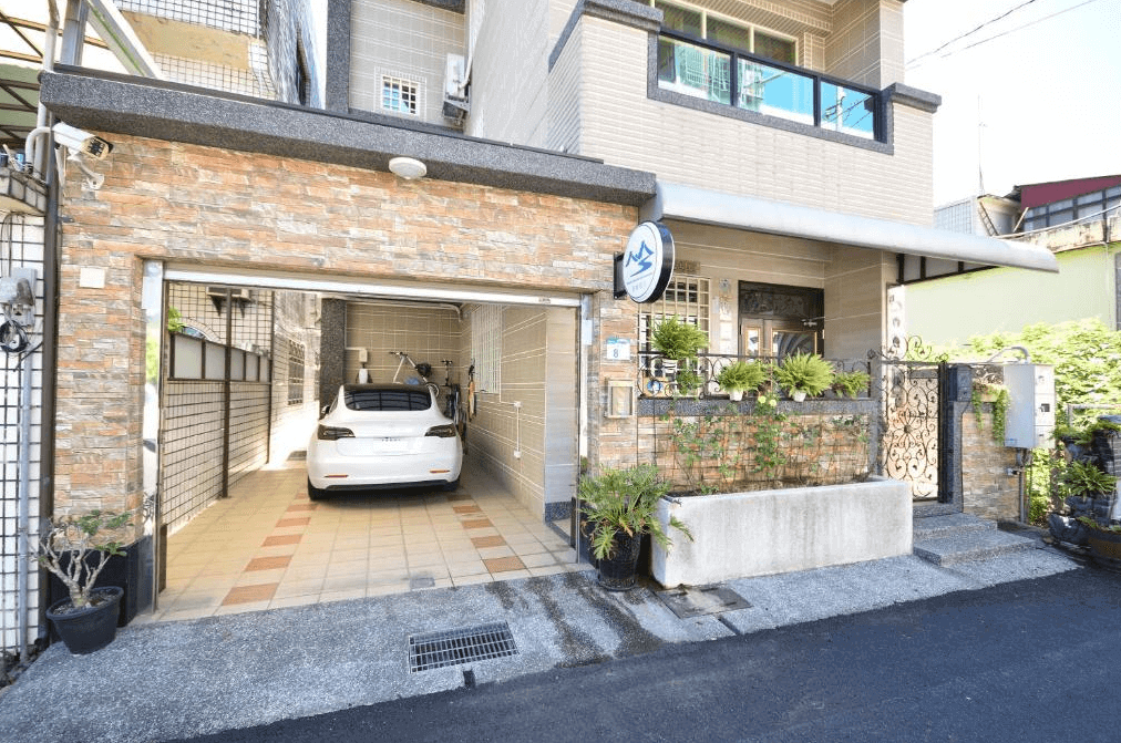 【美濃住宿】望峰息心民宿，建築外觀為現代風格，配有車庫和陽台。車庫內停放著一輛白色汽車，入口處裝飾有綠色植物，環境整潔。