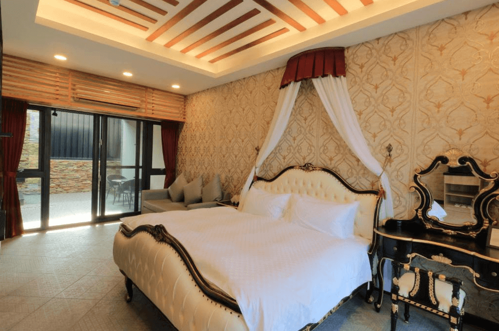東戀溫泉民宿的古典風格臥室，內有一張四柱大床，床頭有華麗的裝飾和帷幔。房間內還設有古典梳妝台和沙發區，整體設計充滿浪漫和優雅的氣息。
