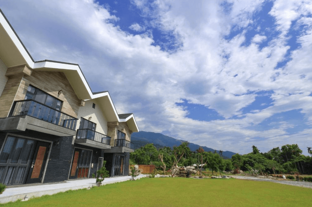 東戀溫泉民宿的外觀，設計現代，前方是一片綠色草地和美麗的山景。建築物有兩層樓，每個房間都有獨立的陽台，住客可以在陽台上享受寧靜的自然風光。