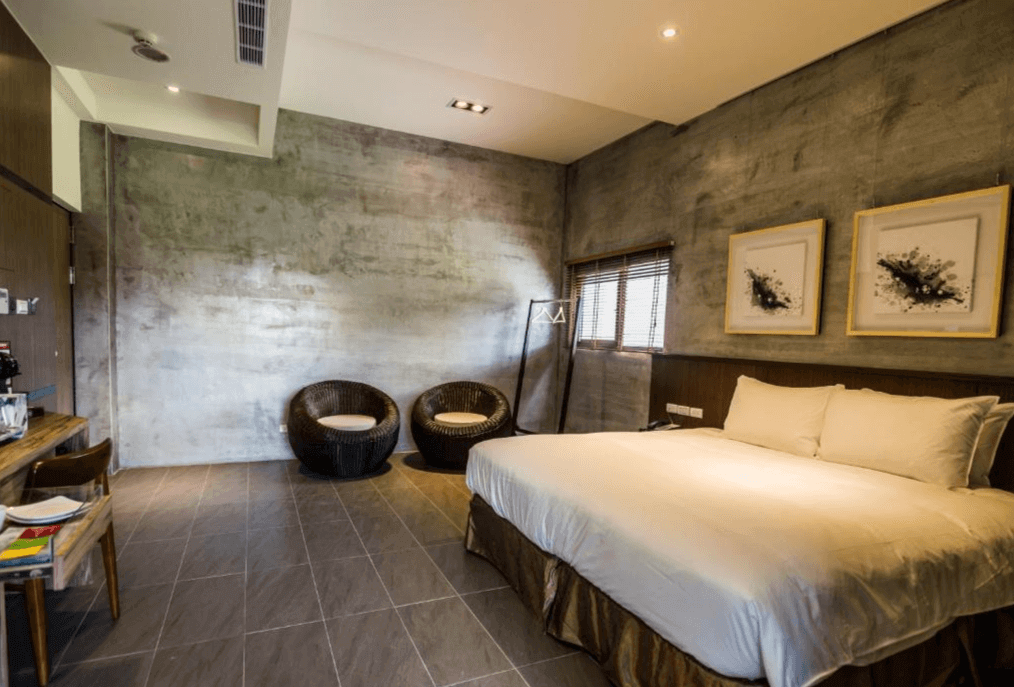 松邑莊園的雙人房，房間內有一張大床，床頭掛有兩幅黑白抽象畫。房間內設有兩張藤椅和一個木製小桌，牆壁呈現灰色水泥質感，營造出現代工業風格。