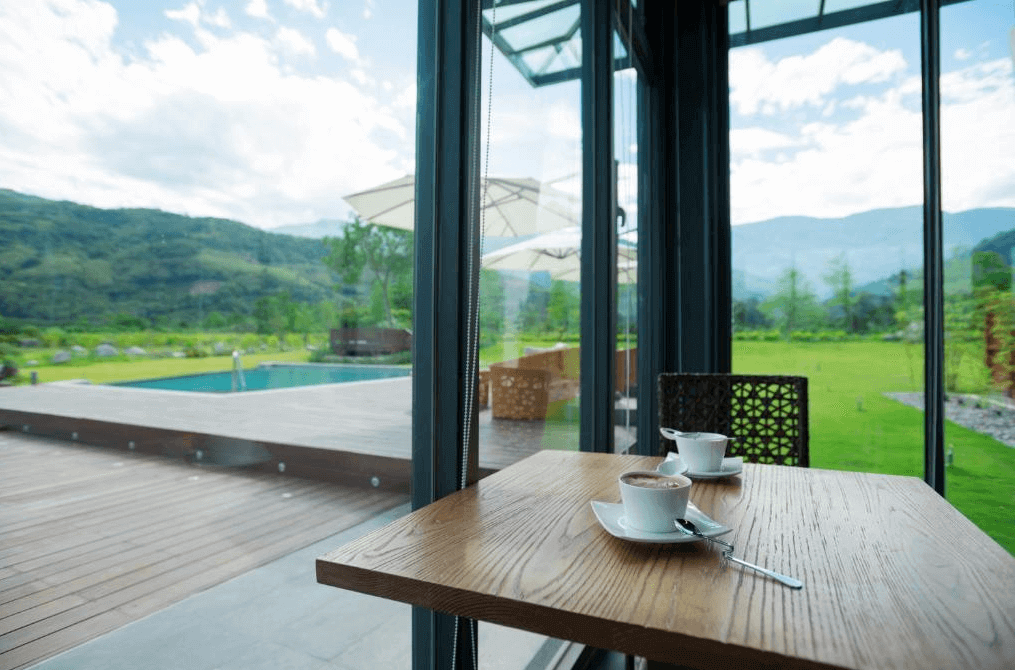 松邑莊園的咖啡桌，桌上擺放著兩杯咖啡，背景是美麗的戶外景觀。通過落地窗可以看到外面的游泳池和綠意盎然的山景，讓住客在享用咖啡時能夠放鬆心情，欣賞自然美景。