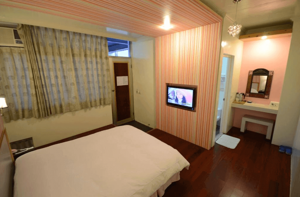 椰子林溫泉飯店的雙人房，內有一張雙人床，牆壁裝飾著粉色和橙色條紋。房間內設有電視和化妝桌，窗戶掛有淡色窗簾，整體氛圍溫暖且舒適，適合情侶或個人入住。