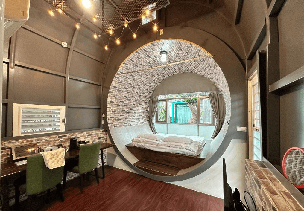 【美濃住宿】美濃涵園民宿房間，房內設計成圓形拱門樣式，內部裝飾有磚牆和木質地板，設有雙人床和工作區。房間氛圍溫馨，適合享受獨特住宿體驗的旅客。