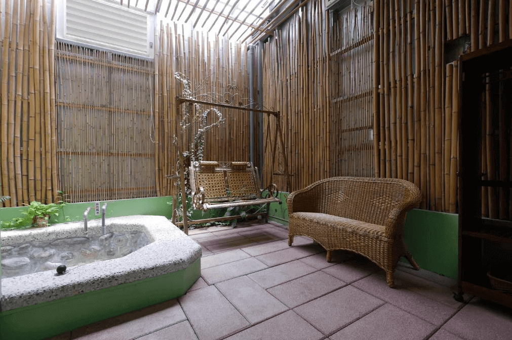 【美濃住宿】美濃涵園民宿的戶外休閒區，設有竹製的牆壁和天花板，配有搖椅和藤製沙發。區域內還有一個小型石製浴池，提供放鬆的空間，讓人感受到自然的氛圍。