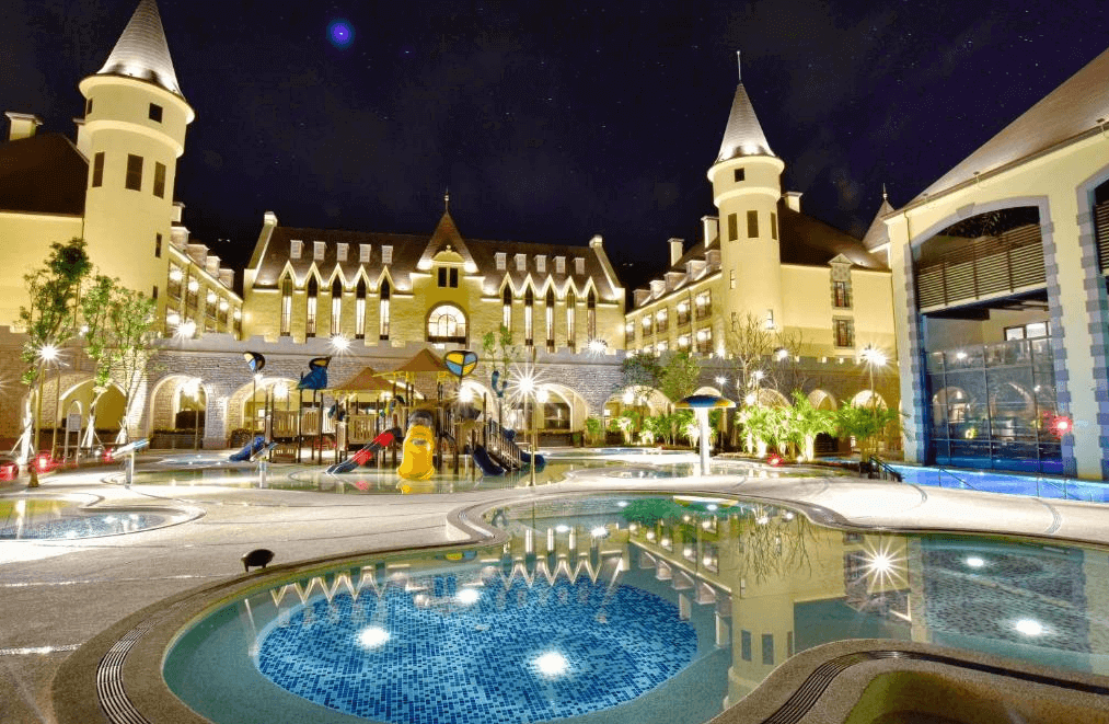 【花蓮寵物友善飯店】瑞穗天合國際觀光酒店的夜景照片，顯示出酒店的外觀和遊泳池區域。酒店外觀仿古典城堡設計，夜間燈光璀璨。遊泳池區域設有各種設施，為住客提供了娛樂和放鬆的場所。背景星空和酒店燈光相輝映，展現出迷人的夜景。