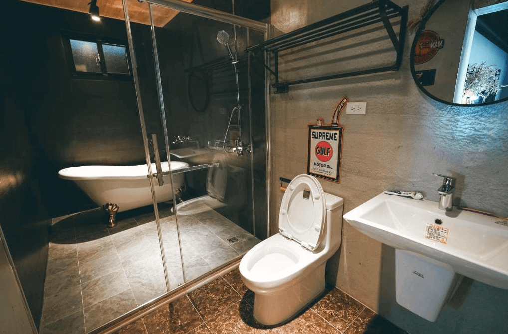 【美濃住宿】美濃煙城民宿的浴室，牆面和地板採用深色瓷磚，配有一個古典風格的獨立浴缸和現代化的淋浴設施。浴室內還設有洗手台和馬桶，整體風格融合了復古與現代元素